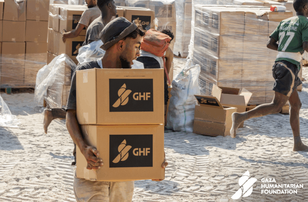 Aid recipients carry Gaza Humanitarian Foundation food boxes.